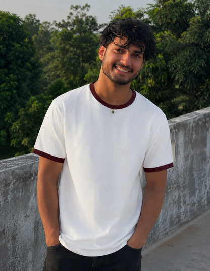 Man wearing a white t-shirt with maroon trim standing outdoors with greenery in the background